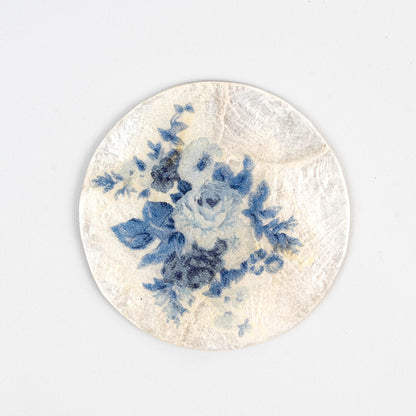 Handcrafted capiz shell coaster with blue floral decoupage design, featuring delicate blue flowers on a cream white background, showcasing sustainable artisanal craftsmanship and eco-friendly materials