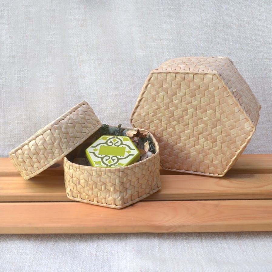 Handcrafted palm leaf hexagonal boxes in natural color, showcasing intricate weaving patterns. One box is open, displaying its interior with a decorative item inside, highlighting the versatility and artisanal quality of the Dese product.