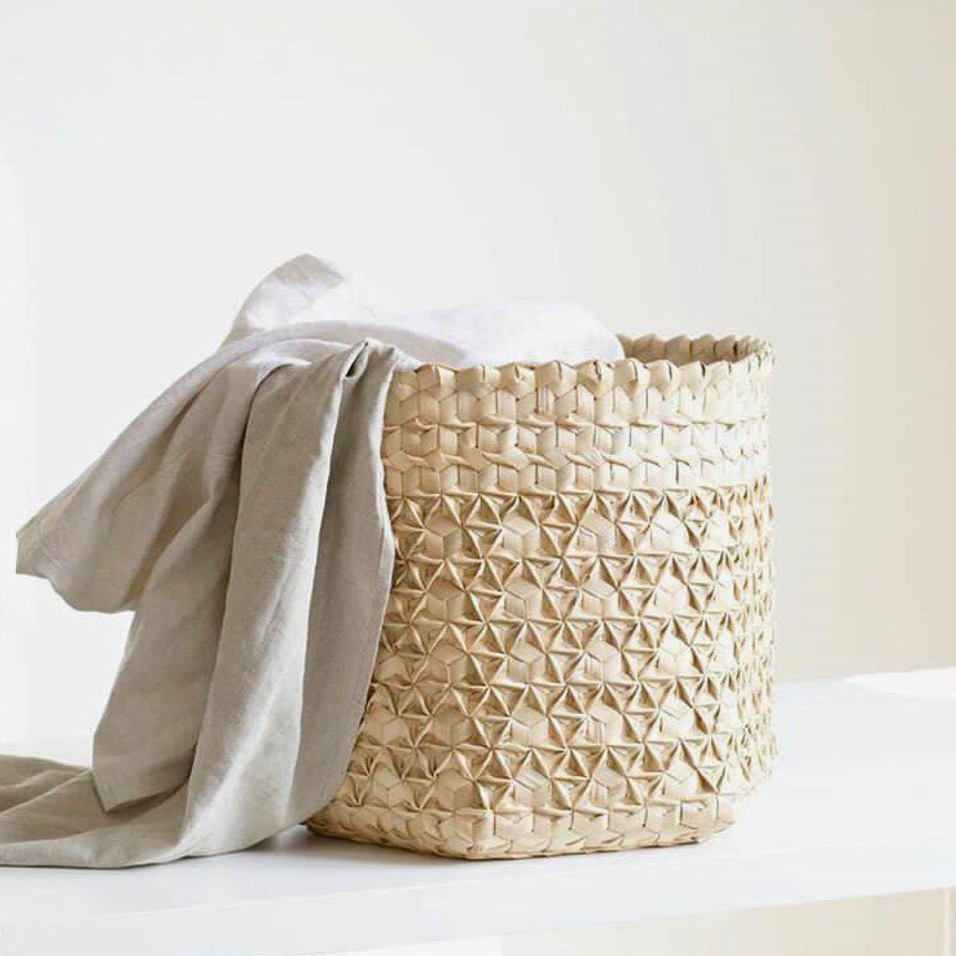 Handwoven palm leaf storage basket with intricate hexagonal pattern, natural color, containing white fabric, showcasing sustainable Indonesian craftsmanship and versatile storage solution for home decor