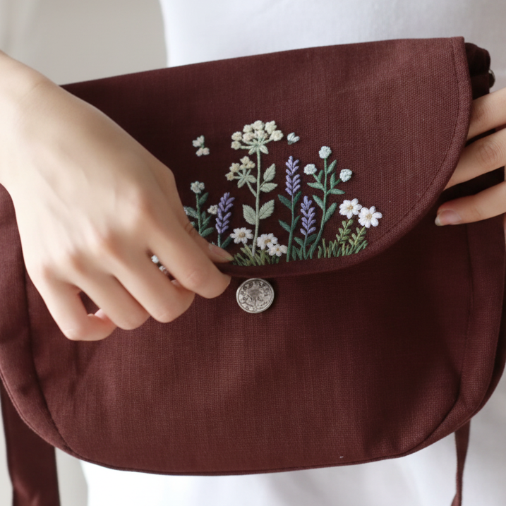 Brown pouch with floral embroidery held by a person against a white background